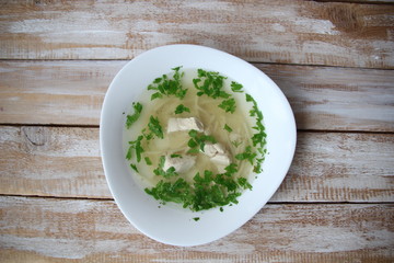 Chiken noodle soup with parsley in white bowl on wooden table