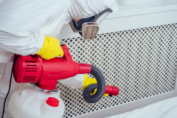 pest control worker lying on floor and spraying pesticides in bedroom