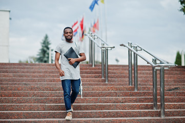 African student male posed with backpack and school items on yard of university, against flags of different countries.