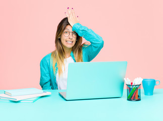 young pretty woman working with a laptop raising palm to forehead thinking oops, after making a...
