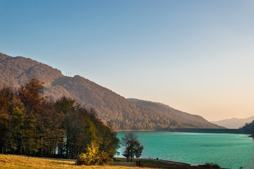 Obraz premium Beautiful view through the trees of a lake surrounded by forests, in a sunny day in autumn
