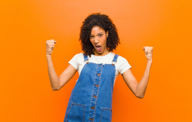 young pretty black woman feeling happy, surprised and proud, shouting and celebrating success with...