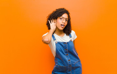 young pretty black woman looking serious and curious, listening, trying to hear a secret...
