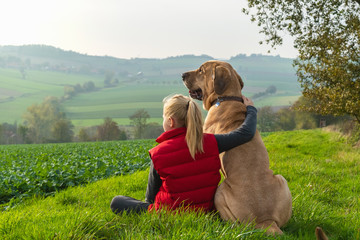 Beste Freunde - ein Mädchen sitzt in der Natur und umarmt seinen besten Freund, einen Broholmer,...