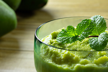closeup of avocado dessert in green glass jar with mint on top over wooden table