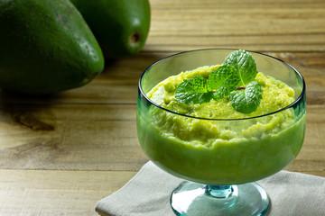 avocado dessert in green glass jar with mint on top over wooden table