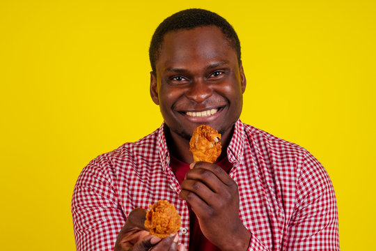 Funny African American Man Eating Fried Chicken Leg In Studio Yellow Background