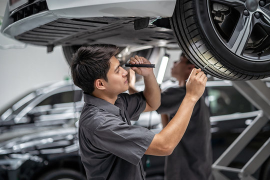Asian mechanic Checking and torch tire in maintainance service center which is a part of showroom, technician or engineer professional work for customer, car repair concept