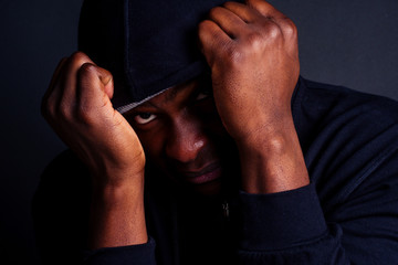 worried young african american mele wearing gray hat and black hoody with hood hiding from the...