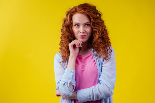 happy thinking redhead ginger curly woman feeling good emotions in studio shot yellow background. language education idea
