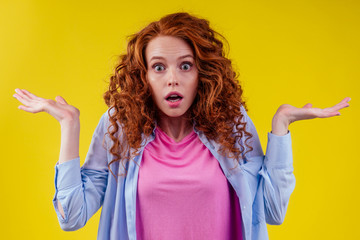 I have no idea.redhaired ginger curly woman arms out shrugs shoulders in studio yellow background - obrazy, fototapety, plakaty