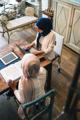 Two young Muslim women study on books and laptop at the kitchen table - Arabian Millennials are preparing for university exams - Top view