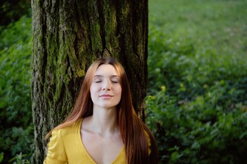 Redhead Woman Leaning On Tree Smiling With Closed Eyes