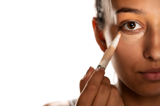 Young dark skinned woman applying concealer on her low eyelids on white background