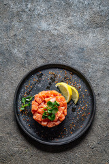 Raw salmon, avocado purple onion salad served in culinary ring on black plate. Black concrete background