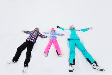 young family of three-mom, dad and daughter lie on the snow in brightly colored ski suits or in winter clothes and make an angel