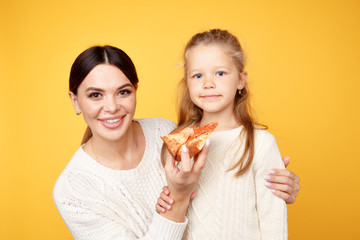 Mother and daughter eating pizza for lunch isolated over the yellow background