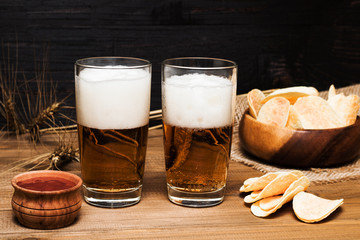 Oktoberfest food menu, beer in a glass on a wooden tray next to traditional snacks: chips and red sauce, on a dark old rustic wooden background, copy space