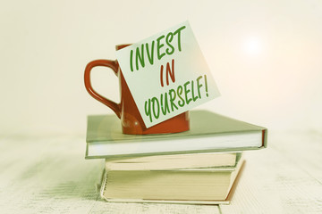 Conceptual hand writing showing Invest In Yourself. Concept meaning learn new things or materials thus making your lot better Coffee cup sticky note stacked books retro old retro wooden table