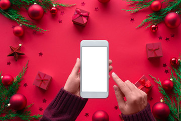 Female hand hold phone on merry christmas red background, girl customer shopper using online mobile shopping app choosing holiday gifts with mobile payments on mock up white screen, close up top view