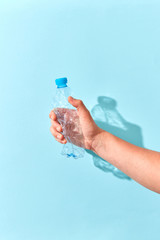 Hand crushes plastic bottle with shadow on a light blue.
