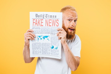 scared bearded man holding newspaper with fake news, isolated on yellow