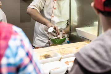 Chef is cooking noodle in bowl for customers who are waiting.