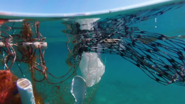 Over under shot of various wasted plastic trapped in the fishing net floats along the coast