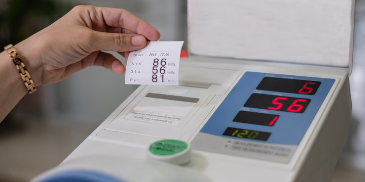 Young woman reading result from arm insertion automatic blood pressure monitor with easy-to-read display.