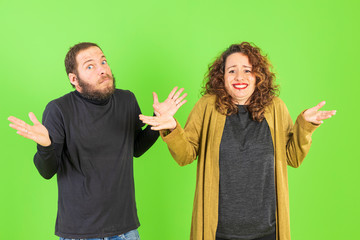 Beautiful young couple confused, trying to take a decision expressing doubt and frustration over green background