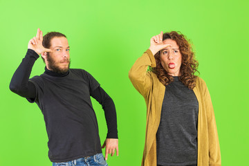 Young crazy couple making funny gestures over green background. LOL symbol.