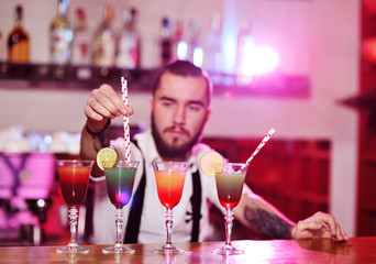 the bartender puts the tubes for cocktails in the prepared alcoholic drinks and smiles against the night club