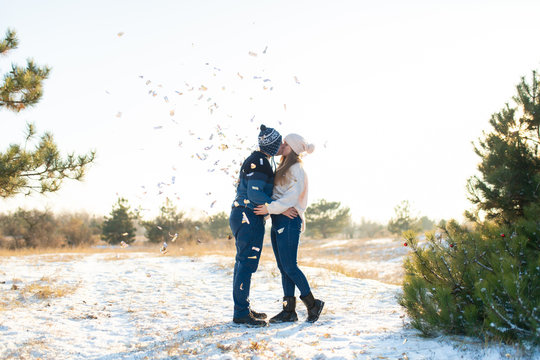 The guy with the girl kiss in the winter in the woods against the background of falling candy. Romantic winter atmosphere