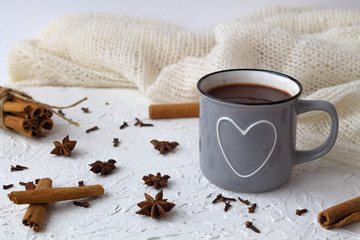 Obraz na płótnie Canvas winter and autumn hot drinks. grey cup of hot chocolate or cocoa and cinnamon, anise star with knitted white plaid on white background. copy space.