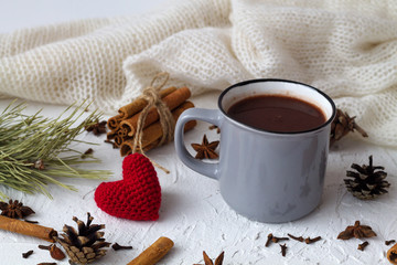 grey cup of hot chocolate and cinnamon, anise star and knitted red heart with pine cone and green spruce branch on white background. horizontal. winter and autumn hot drinks