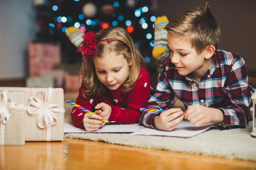 Two happy children writing letter to Santa Claus at home near New Year tree