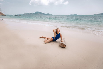 Young attractive blonde woman in a blue swimming suit lying on a sandy beach against the sea background. Summer vacation concept