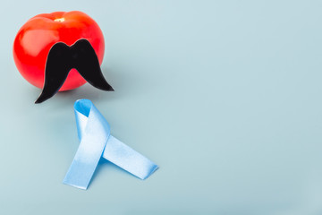 Blue ribbon and tomato with black fake paper moustaches on a blue background as a symbol of...