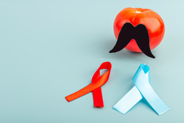 Blue and red ribbons and tomato with black fake paper moustaches on a blue background as a symbol...