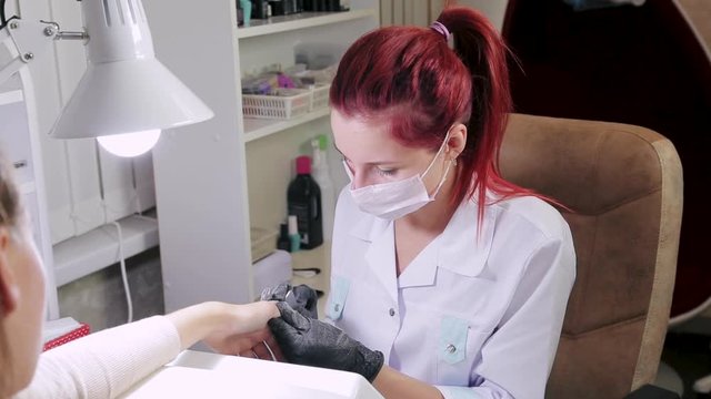 Woman manicurist with gloves in a beauty salon nails a client with a nail file before applying gel coating.