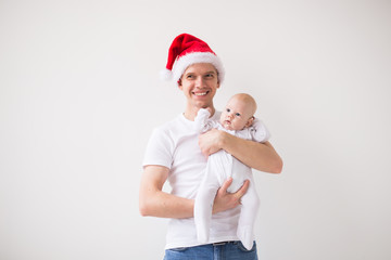 Fototapeta premium My first Christmas. Dad in santa hat holding his baby girl daughter on white background with copy space