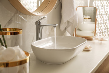 Sink with running water in stylish bathroom interior