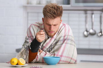 Sick young man eating soup to cure flu at table in kitchen