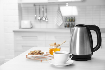 Fototapeta na wymiar Modern electric kettle, cup of tea and cookies on wooden table in kitchen