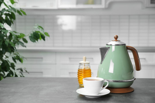 Modern electric kettle, cup of tea and honey on grey table in kitchen