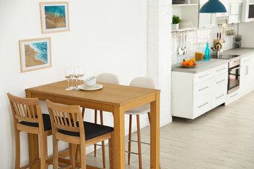 Stylish kitchen interior with dining table and bar stools near white wall