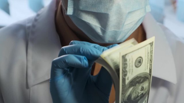 Satisfied doctor with dollar bills in his hands, close-up. concept of doctors earnings, transplantology, corruption in medicine