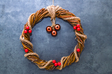Christmas balls for the Christmas tree and a homemade Christmas wreath of twigs with holly berries and jute rope on a gray concrete background.