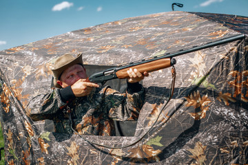 Man standing in ambush in the khaki tent, aiming to the sky; huntsman concept.