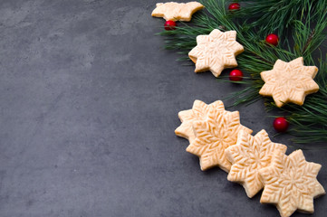 Gingerbread in the shape of a snowflake and a branch of the Xmas tree on a gray background.
